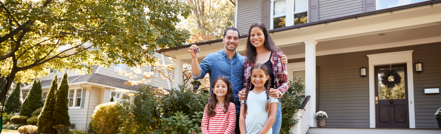 A family of four stands outside their new house.
